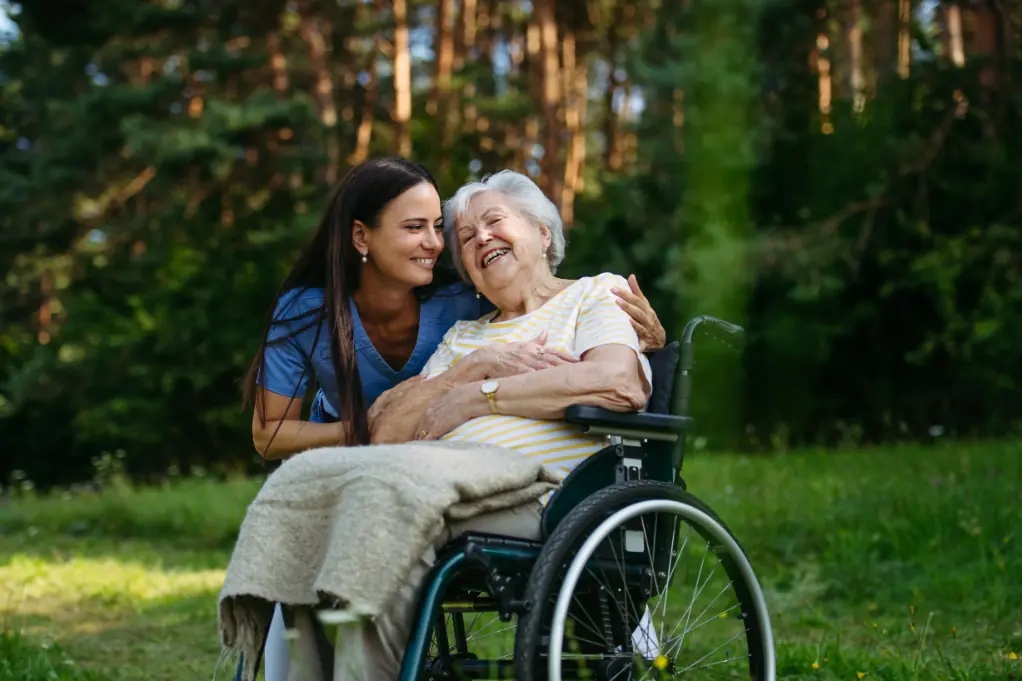 A MedicalOne Health home care nurse in blue scrubs smiling and interacting with an elderly female patient in a wheelchair.